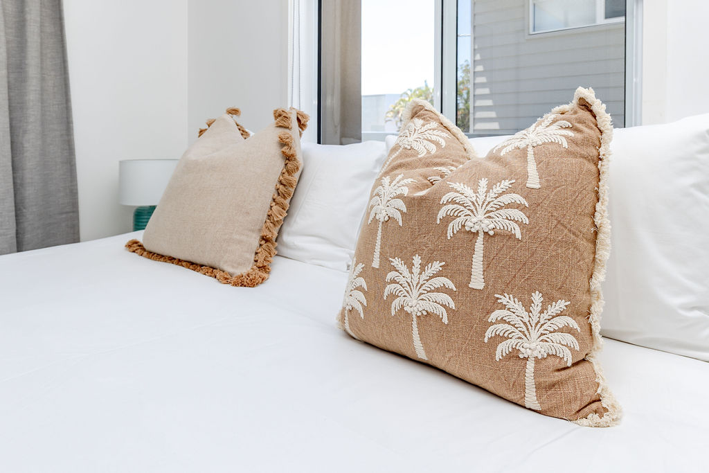 Palm tree embroidered cushions on a crisp white bed